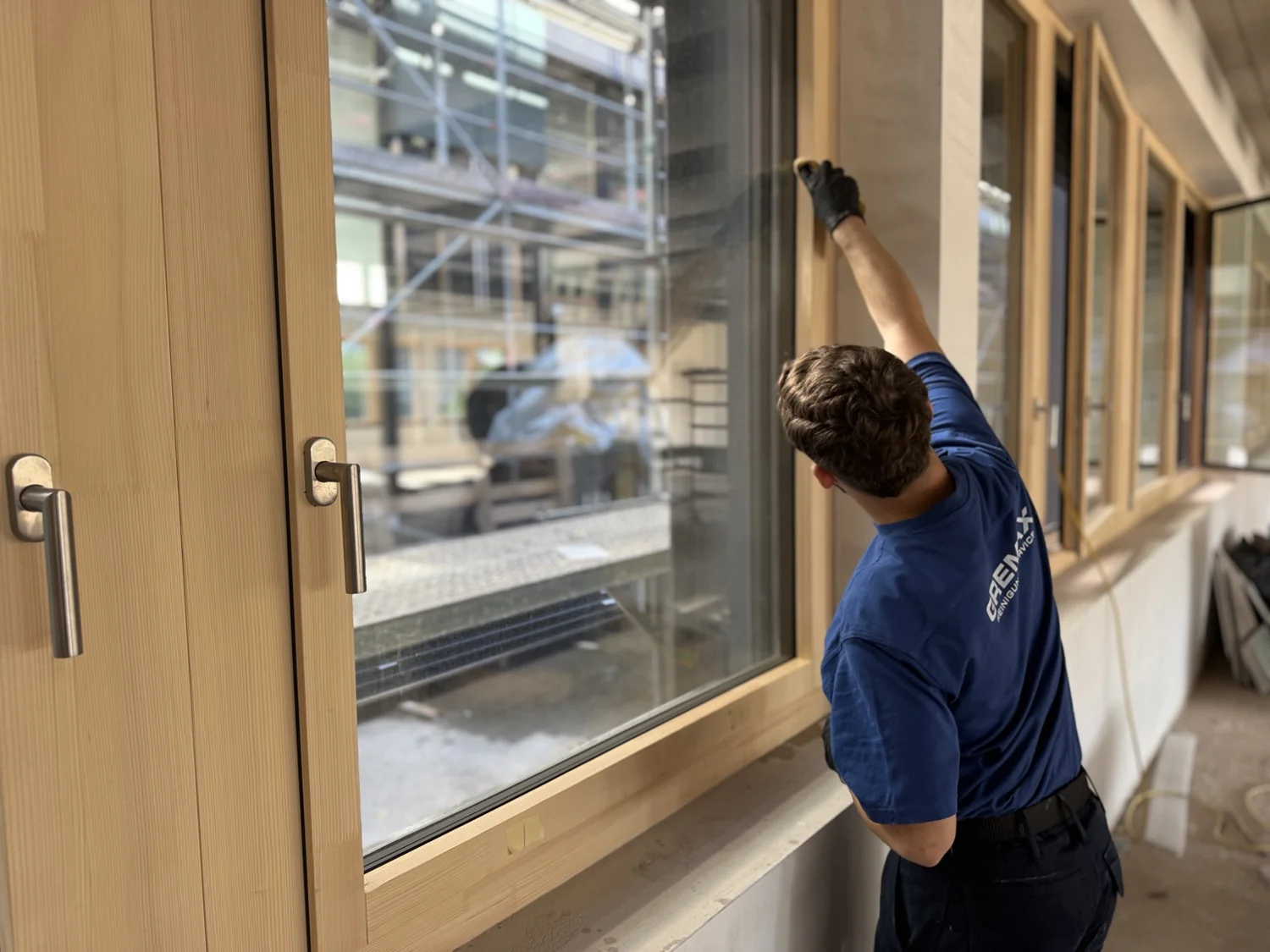 Gremax-Mitarbeiter reinigt ein Fenster mit Holzrahmen