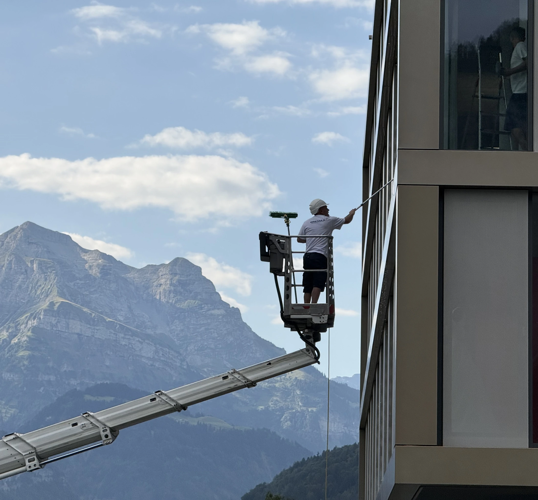 GREMAX-Mitarbeiter reinigt auf einer Hebebühne die Fassade vor einem Bergpanorama